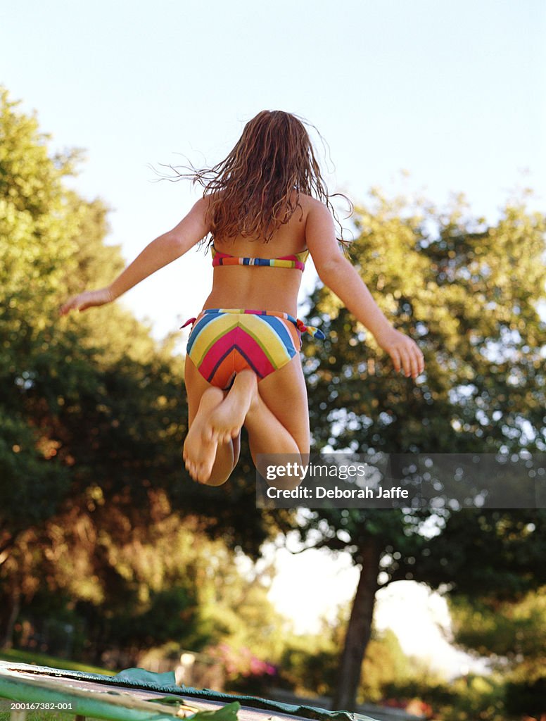 Girl (9-11) wearing bathing suit, jumping, rear view
