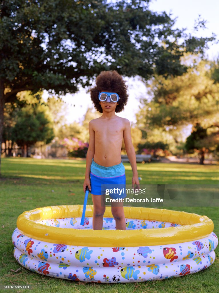 Boy (7-9) wearing goggles, standing in paddling pool