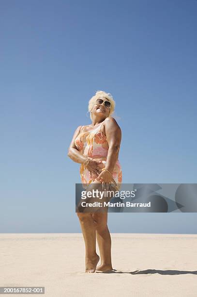 senior woman standing on beach wearing bikini and sunglasses, portrait - old woman in swimsuit stock pictures, royalty-free photos & images
