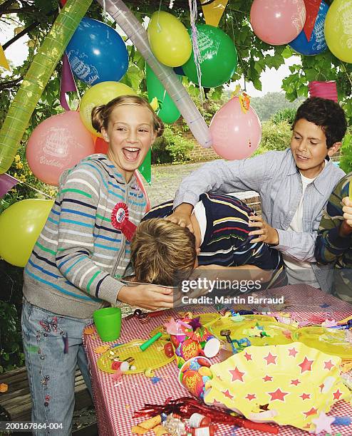 children (9-12) at birthday party, boy pushing other's face into cake - food fight stock pictures, royalty-free photos & images