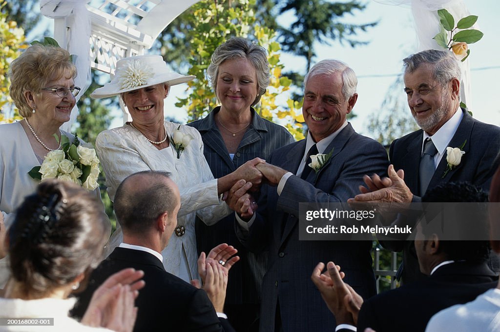 Senior bride and groom holding hands after ceremony, guests applauding