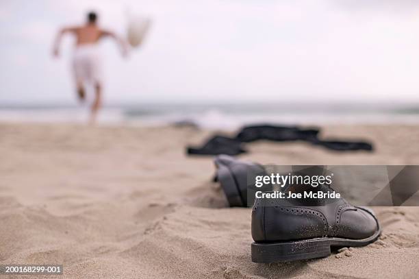 businessman running on beach, shoes and clothes on sand - dress shoe imagens e fotografias de stock