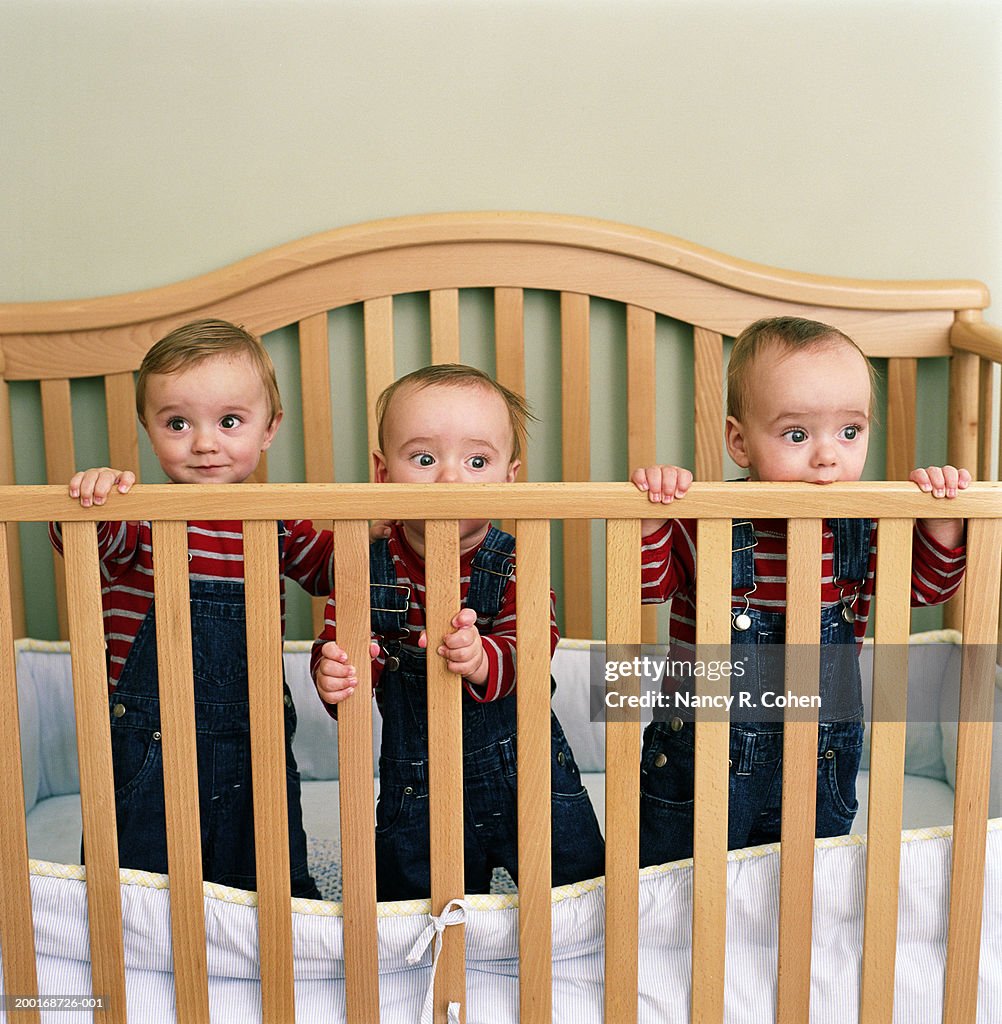 Triplet baby boys (9-12 months) standing in crib