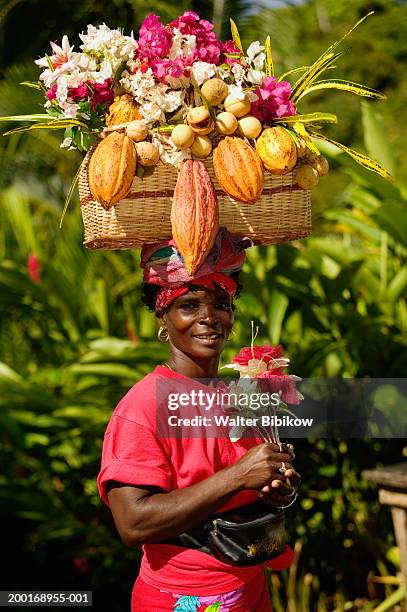 mature woman carrying basket of fruit on head, smiling, portrait - cultura caraibica foto e immagini stock