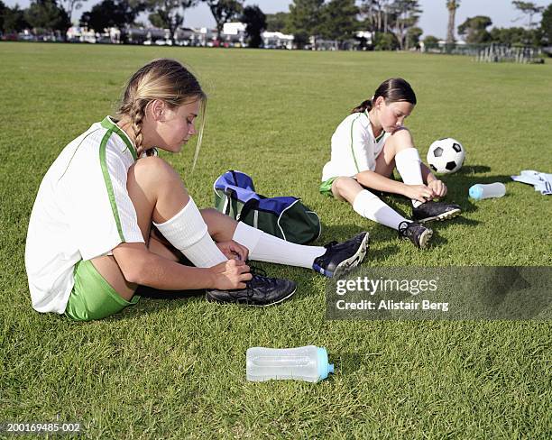 girls (11-13) sitting in field, tying laces on football boots - studded stock pictures, royalty-free photos & images