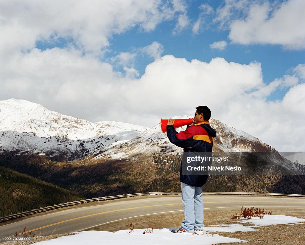 Young man using bullhorn on mountain pass, side view