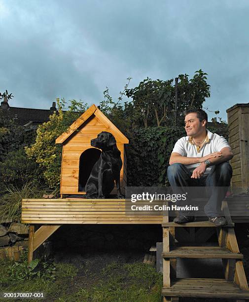 dog sitting outside kennel in garden, man sitting on steps nearby - dog kennel stock pictures, royalty-free photos & images