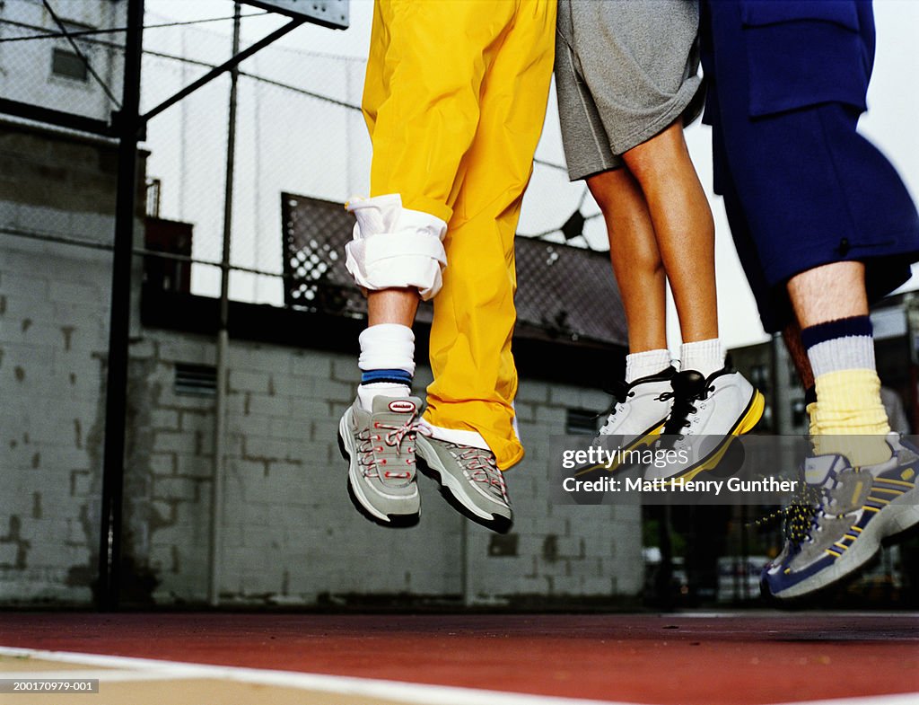 Three people jumping in air on basketball court, low section