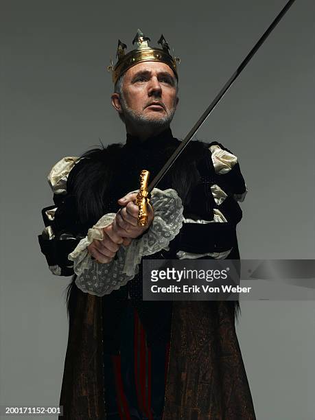 senior man wearing king costume holding sword, and looking away - head of state stock pictures, royalty-free photos & images