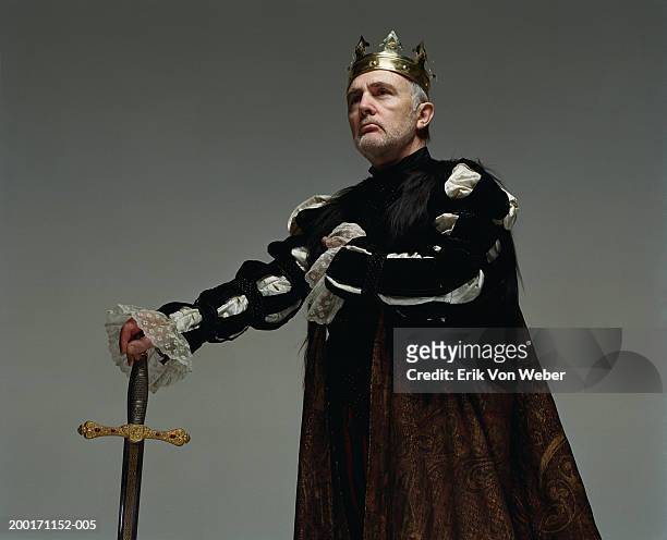senior man  wearing king costume with sword, and looking away - könig königliche persönlichkeit stock-fotos und bilder