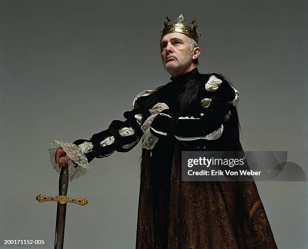 senior man  wearing king costume with sword, and looking away - koning stockfoto's en -beelden