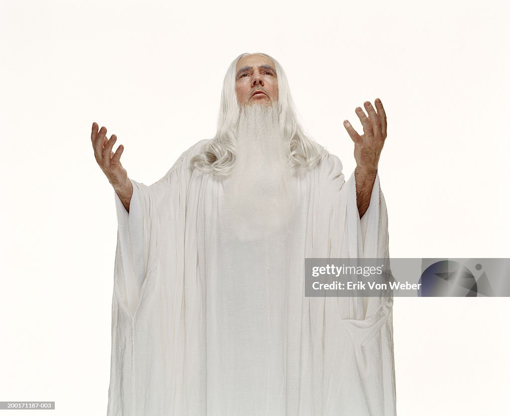 Senior man wearing white robe with hands in air, looking up