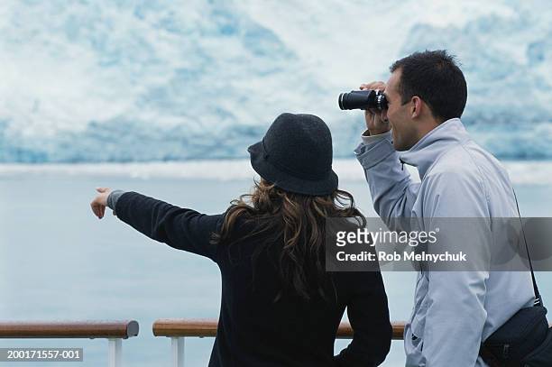 young couple on balcony of ship, man using binoculars, woman pointing - woman looking through ice stock pictures, royalty-free photos & images