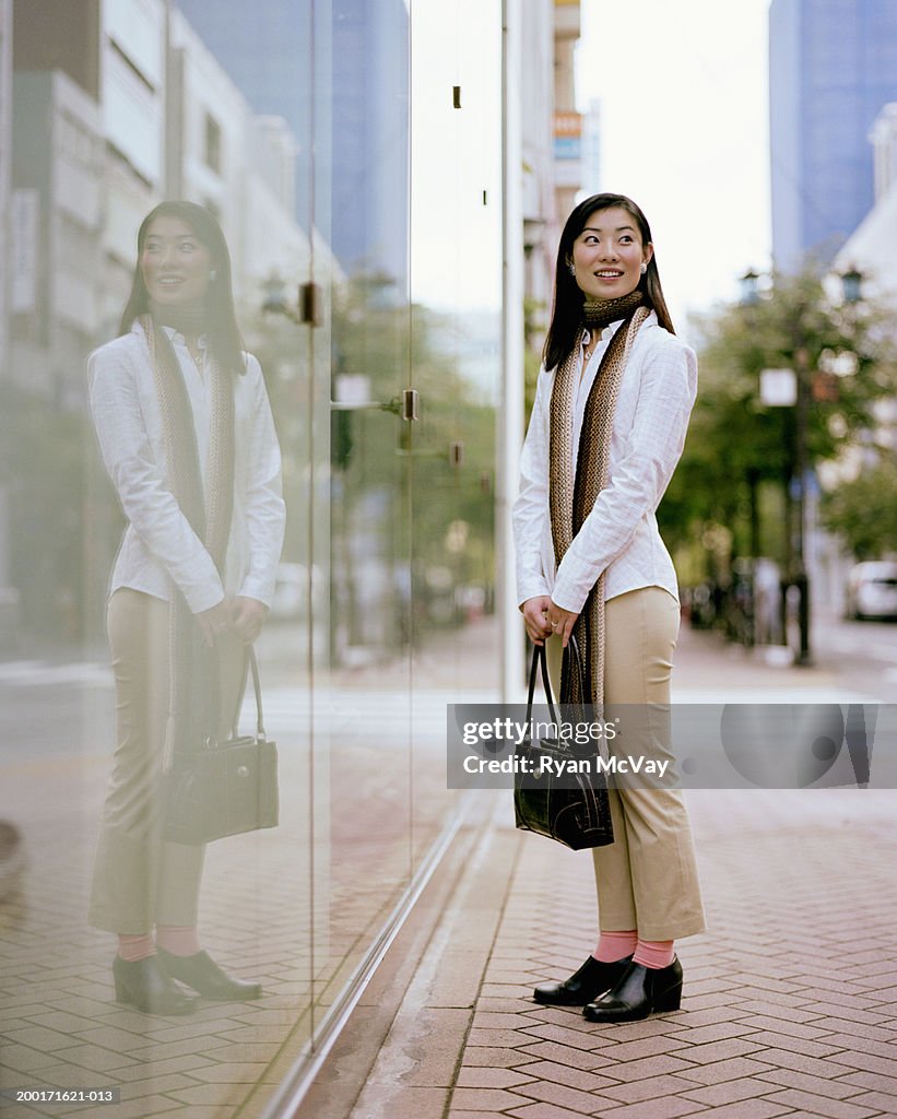 Young woman standing on urban sidewalk, looking over shoulder, smiling