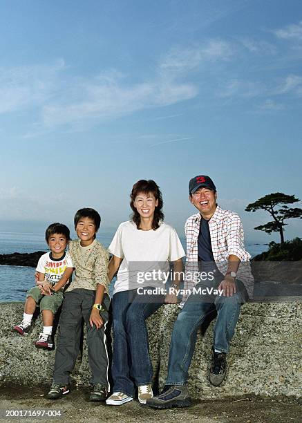 parents and two sons (5-10) sitting on rock wall beside sea, portrait - front view portrait of four children sitting on rock stock-fotos und bilder