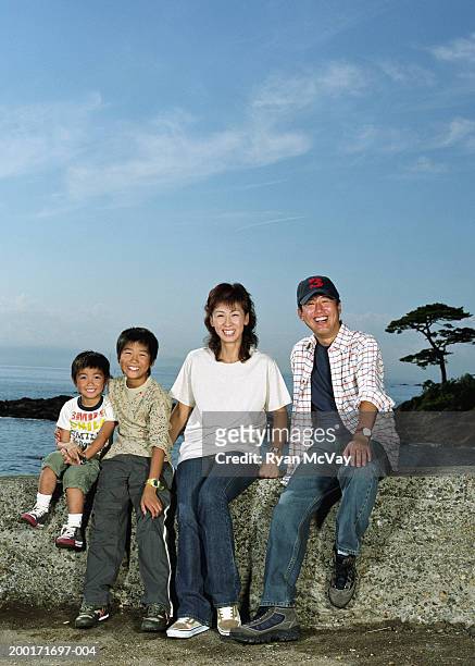 parents and two sons (5-10) sitting on rock wall beside sea, portrait - front view portrait of four children sitting on rock stock pictures, royalty-free photos & images