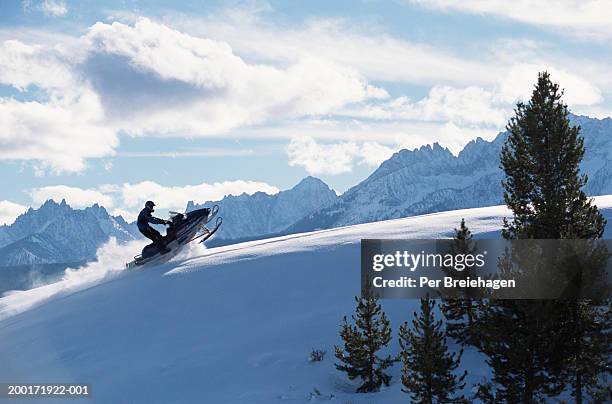 man on snowmobile ascending slope, side view - snowmobiling stock pictures, royalty-free photos & images