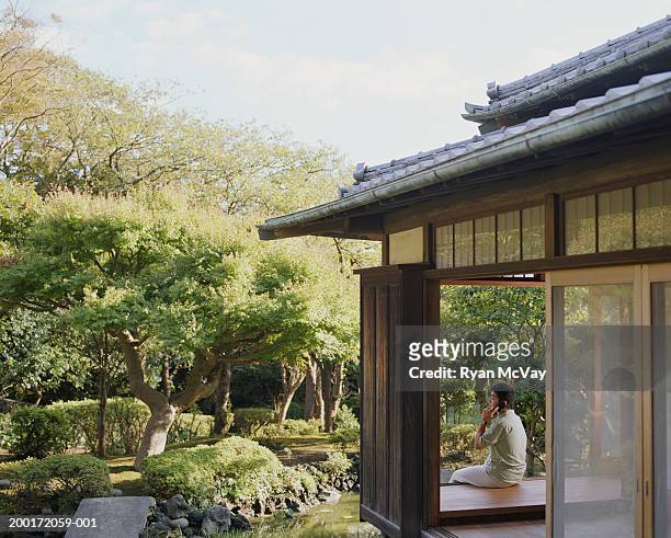 junger mann sprechen auf handy im zimmer mit blick auf - in a japanese garden stock-fotos und bilder