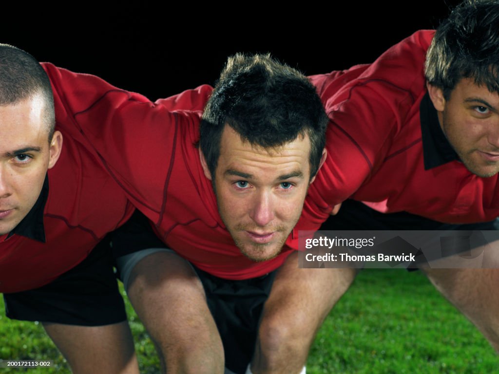 Three young male rugby players in scrum, night, close-up