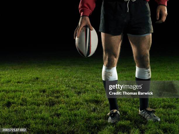 male rugby player holding ball, night, low section - rugbyball stock-fotos und bilder