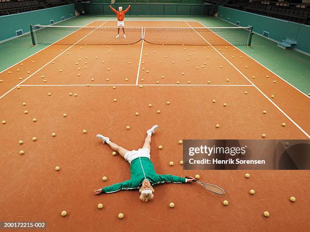 two men either side of tennis court, one lying on ground amongst balls - failure foto e immagini stock