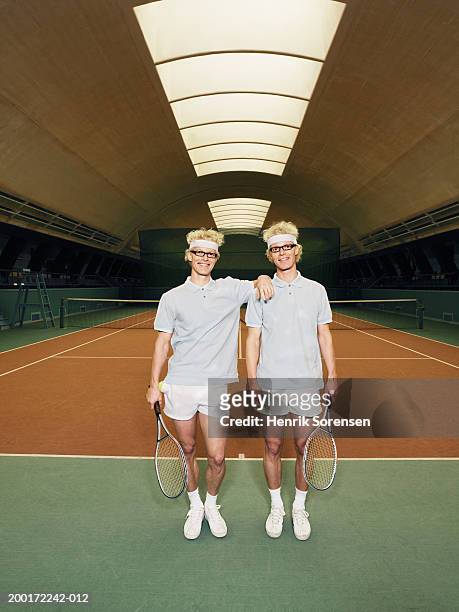 identical male twins holding rackets by tennis court - match sport stockfoto's en -beelden