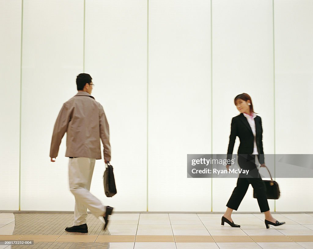 Man and woman walking down corridor, looking over shoulders, side view