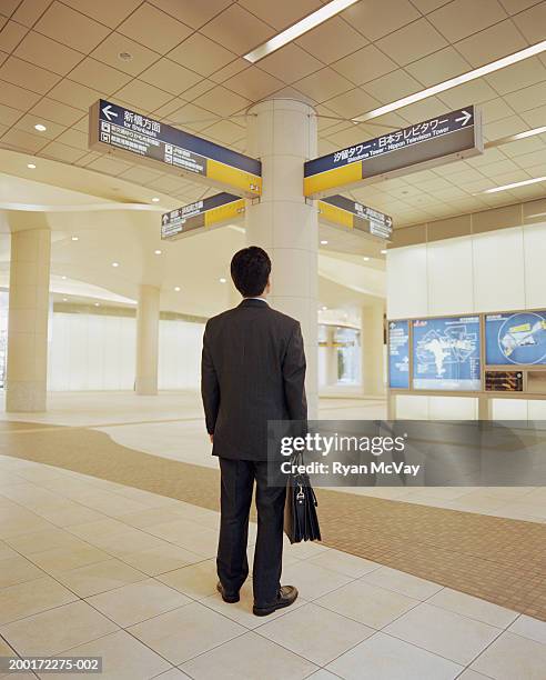 businessman looking at directional signs in subway station, rear view - mann anzug von hinten stock-fotos und bilder