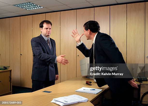 businessman making hand gesture across desk to male colleague - middle finger funny 個照片及圖片檔