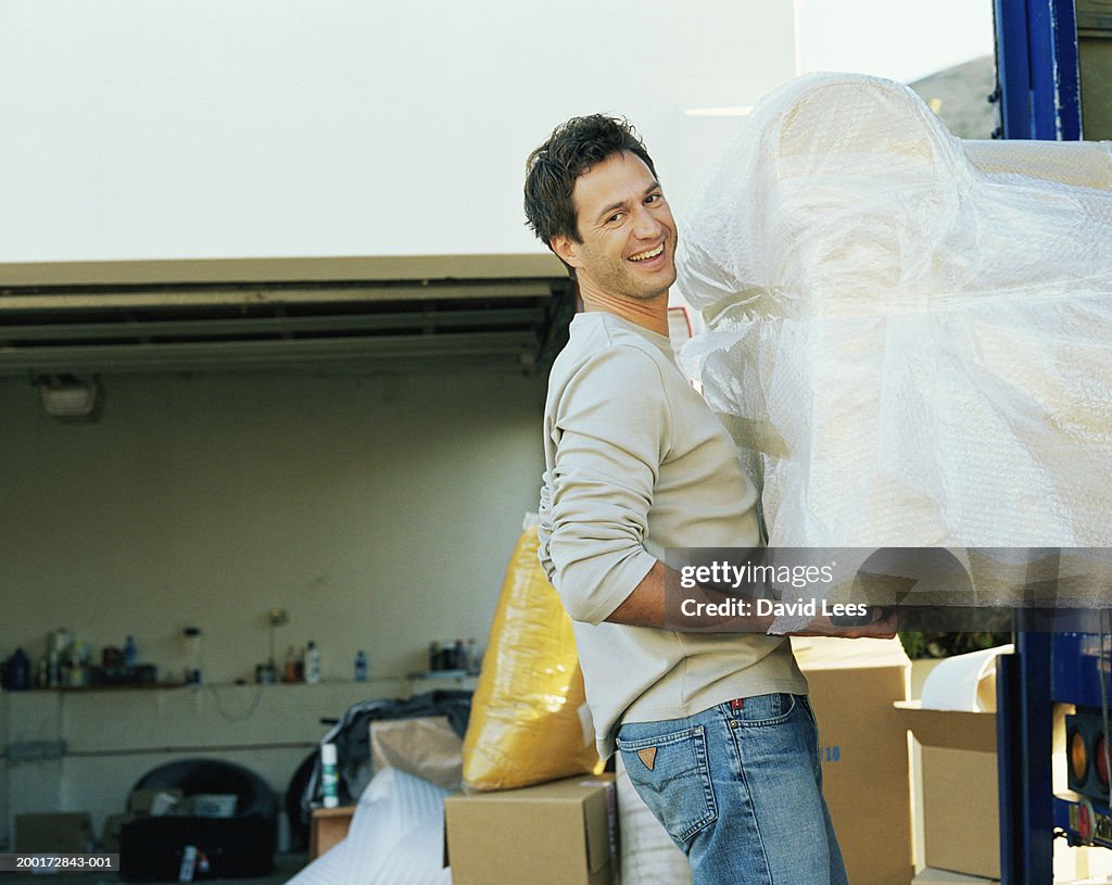 Man loading sofa into removal van, smiling, portrait, side view