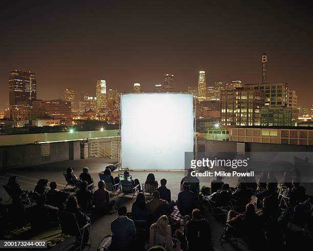 people on rooftop at night, sitting in front of projection screen - filmindustrie stock-fotos und bilder