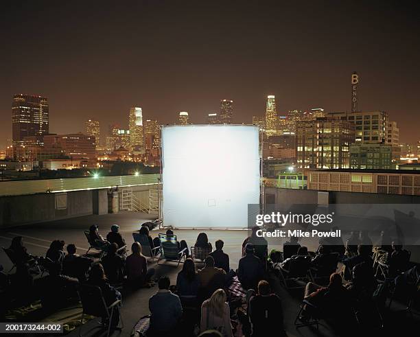 people on rooftop at night, sitting in front of projection screen - outside cinema stockfoto's en -beelden