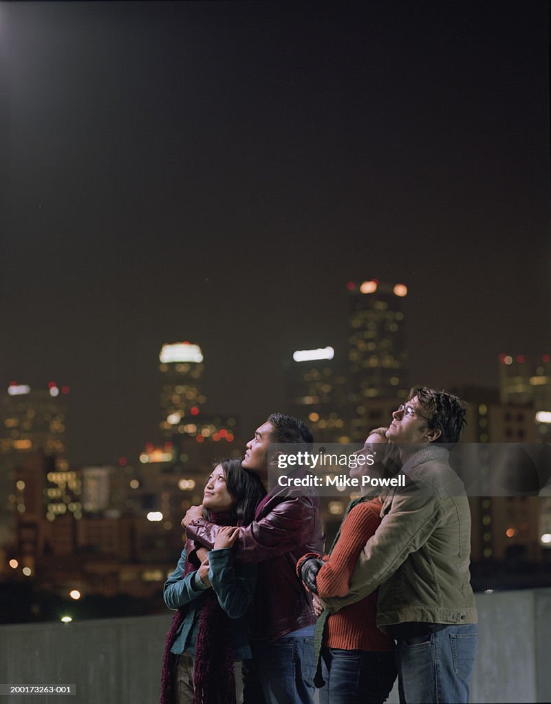 Two couples on rooftop, looking upwards at night sky
