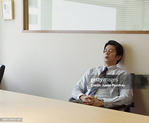 mature businessman relaxing in chair at conference table, eyes closed - tense board meeting foto e immagini stock