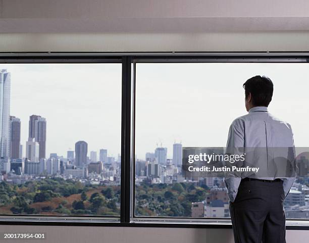 mature businessman looking out window at cityscape, rear view - blue shirt back stock pictures, royalty-free photos & images