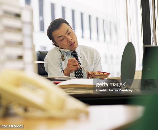 businessman eating lunch at desk, using mobile phone - worker lunch foto e immagini stock