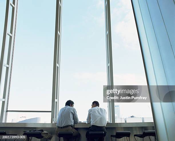 two businessmen in discussion by window, rear view - big city fotografías e imágenes de stock