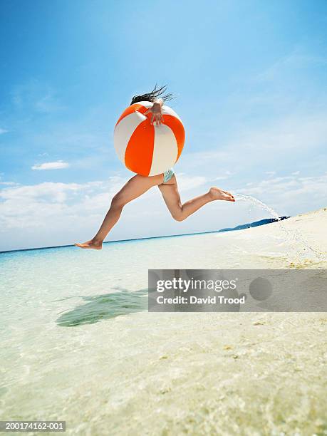 woman holding large beach ball, in air above ocean, side view - unter dem arm stock-fotos und bilder