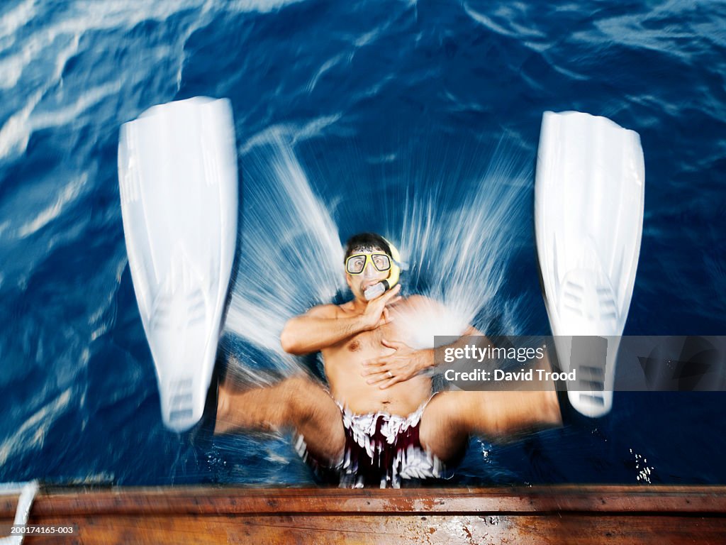 Man wearing snorkel and fins, falling from boat into water, portrait
