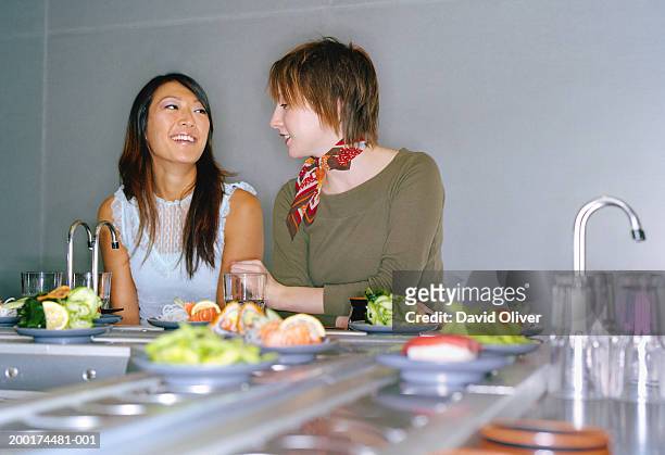 two young women at sushi bar, smiling - sushi train stock pictures, royalty-free photos & images