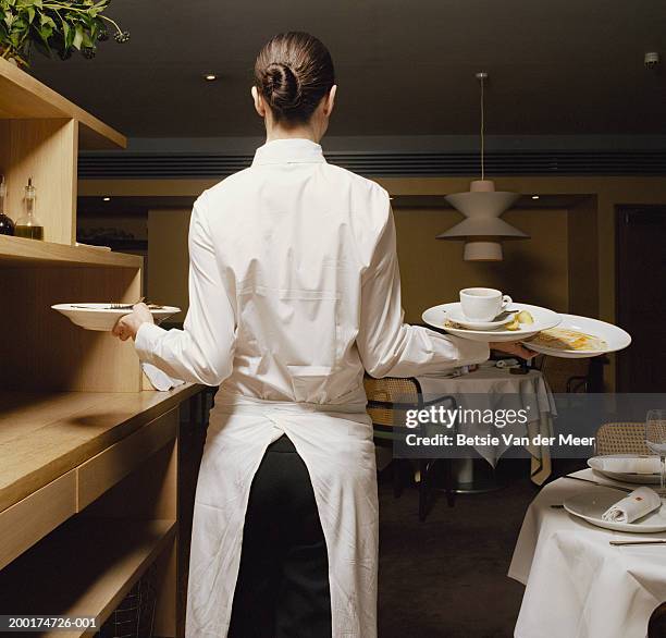 waitress carrying dirty plates in restaurant, rear view - waitress foto e immagini stock