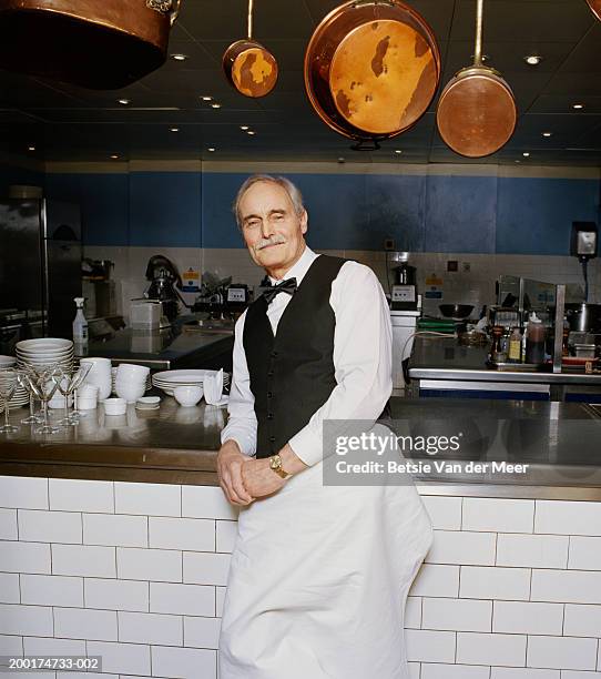 senior waiter leaning on kitchen bench, smiling, portrait - stoneplus10 photos et images de collection