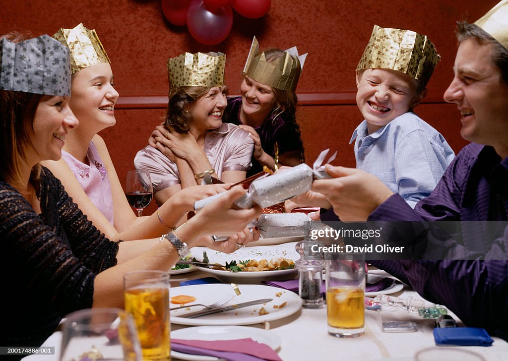 Family at dinner table, wearing party hats, opening christmas crackers