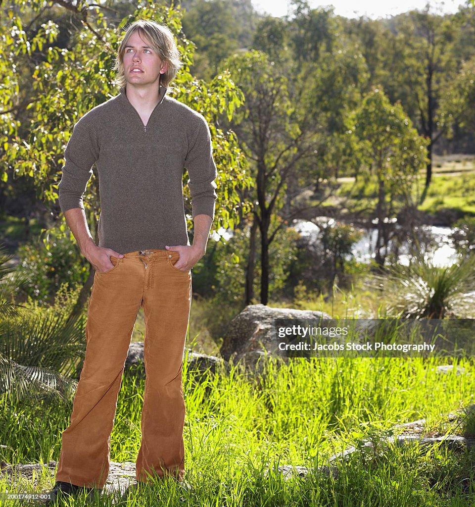 Young man standing in woodland, with hands in pockets, looking to side