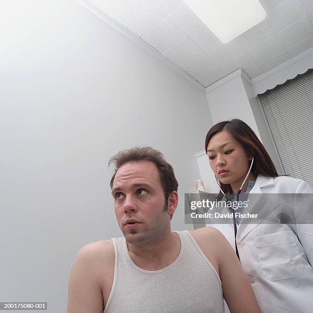 female doctor using stethoscope on man's back, low angle view - unterhemd stock-fotos und bilder