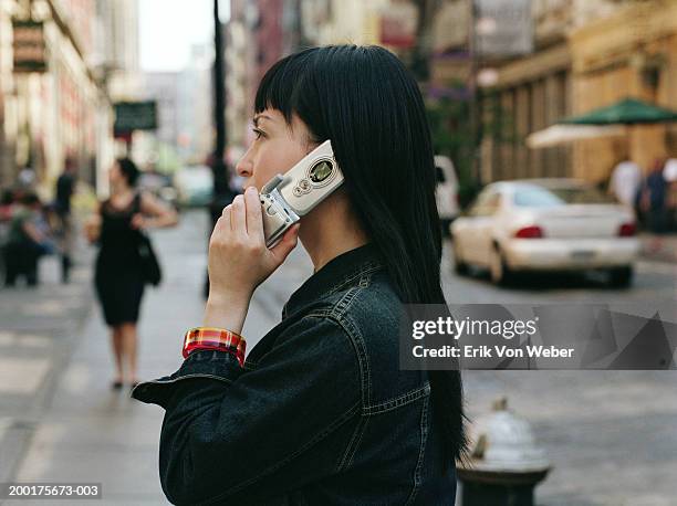 young woman on street using mobile phone, side view - feature phone stockfoto's en -beelden