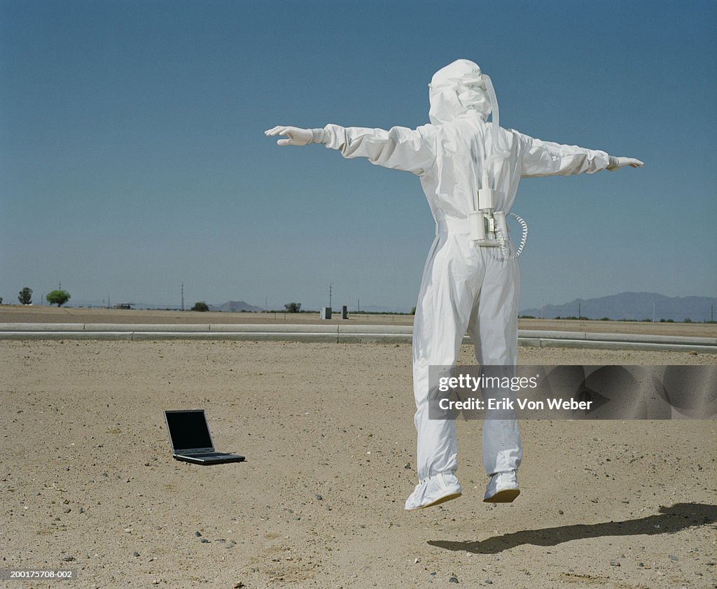 Man wearing protective suit jumping in front of laptop, rear view