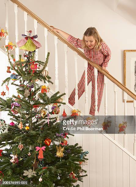 girl (6-8) on staircase railing, looking down at christmas tree - christmas tree stockfoto's en -beelden