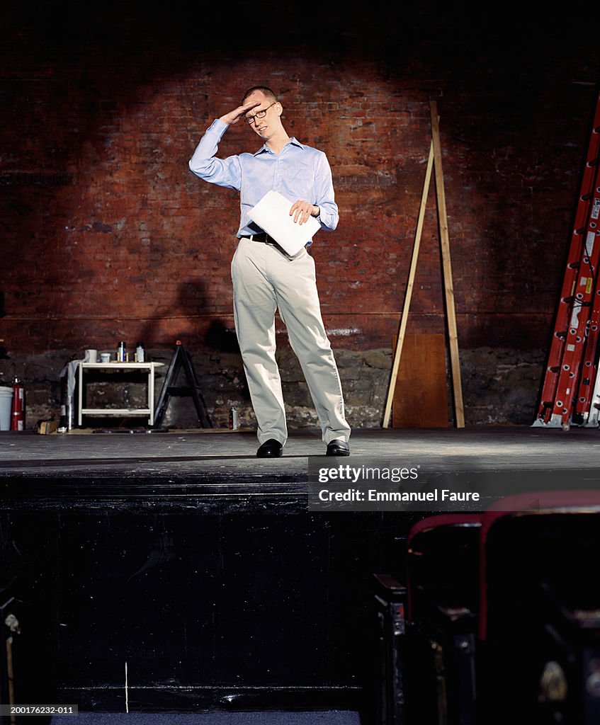 Man on stage in theater with hand on forehead