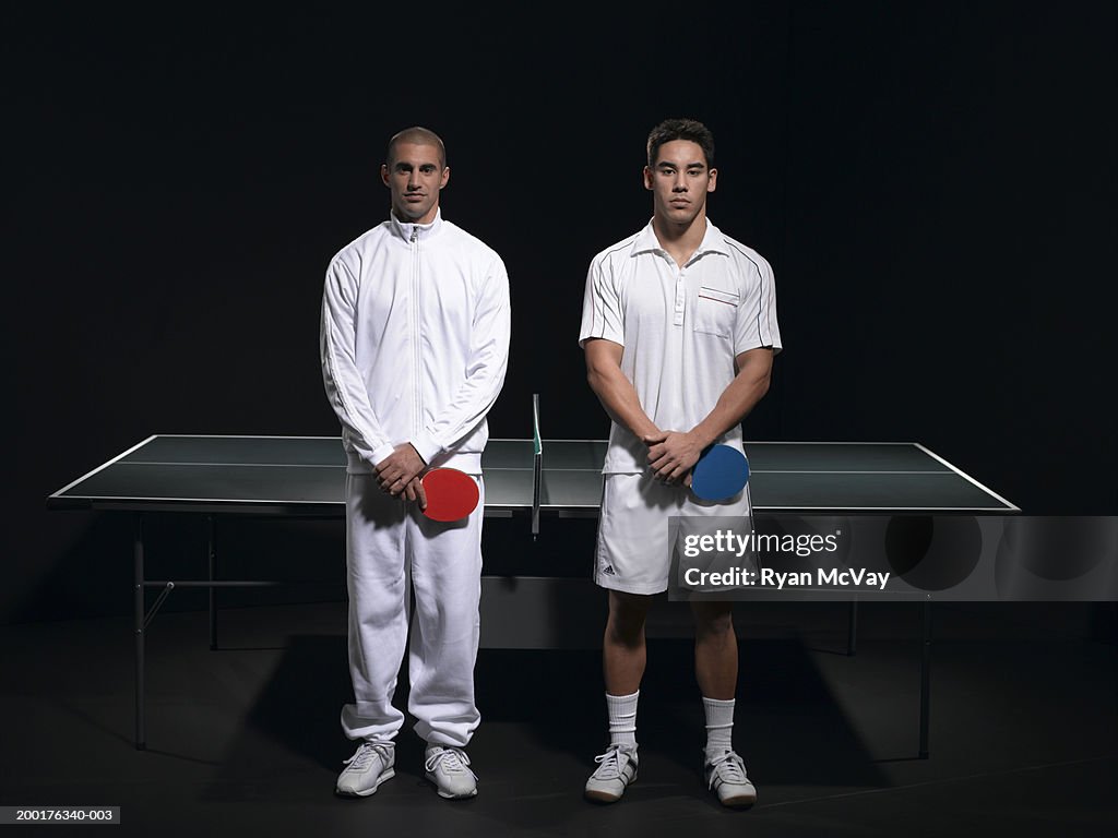 Two young men standing on opposite sides of table tennis net, portrait